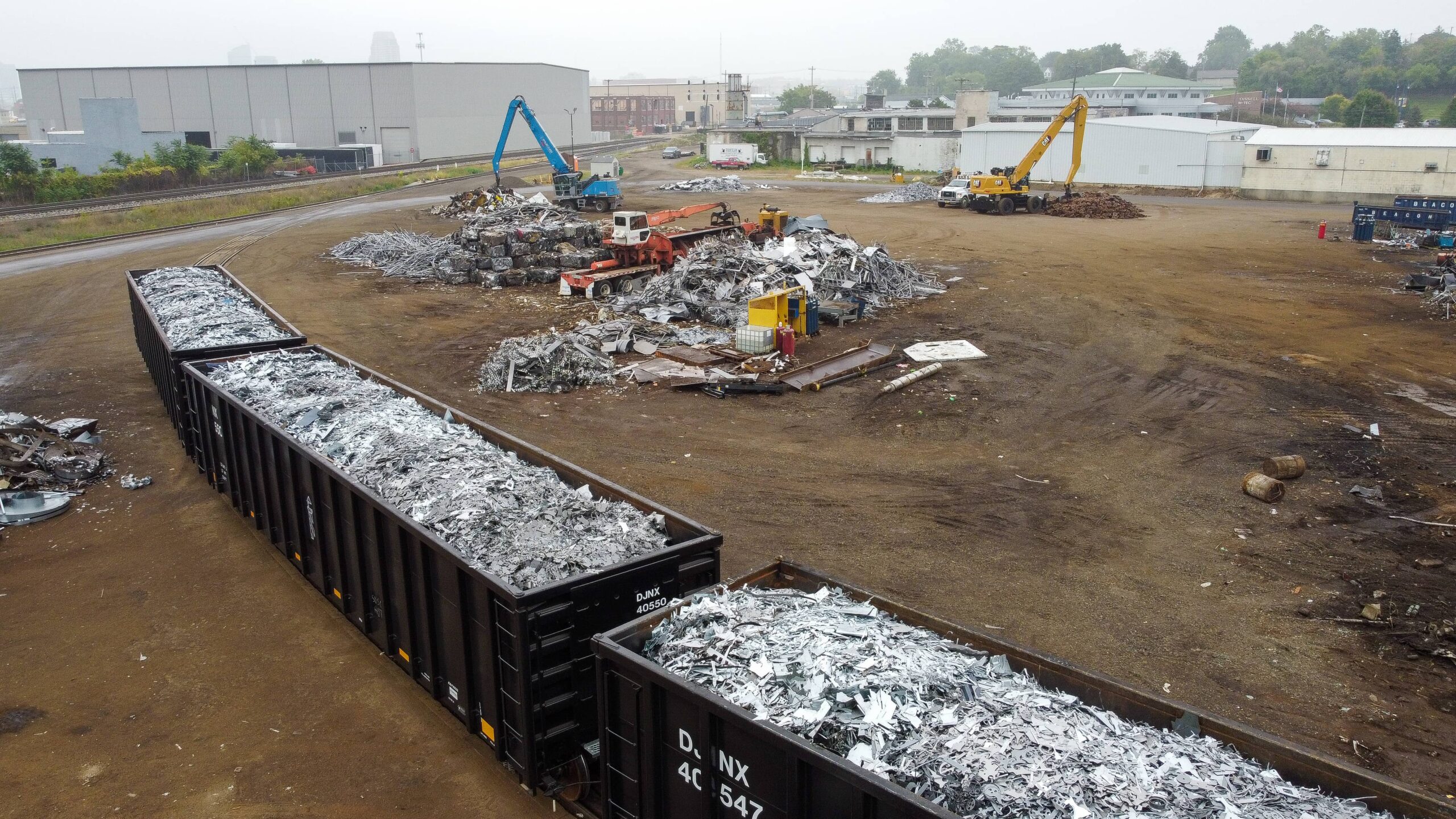 Rail cars filled with shredded metal next to scrap piles and yard equipment