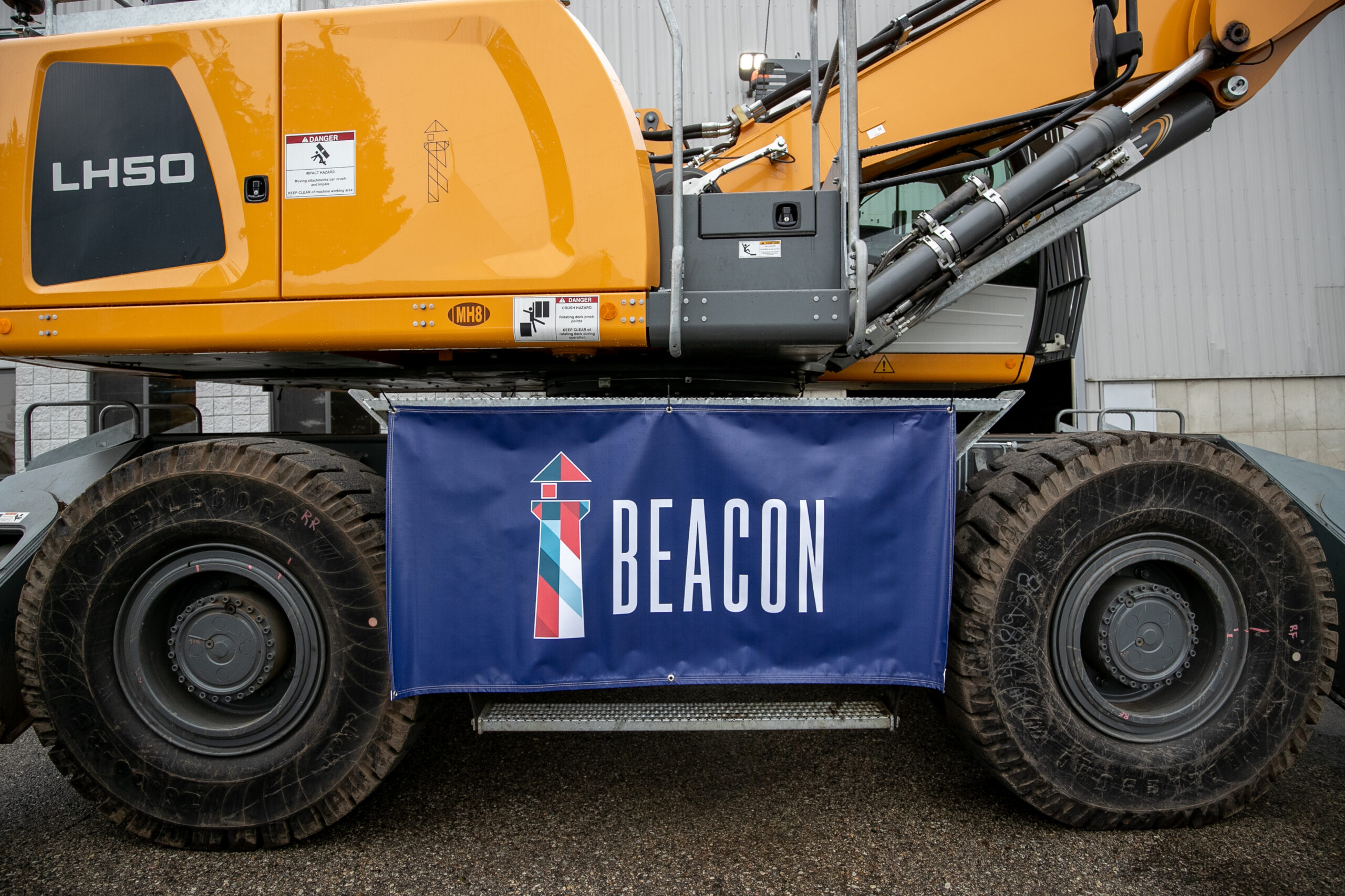 Wheeled material handler with a Beacon banner parked at a scrap yard